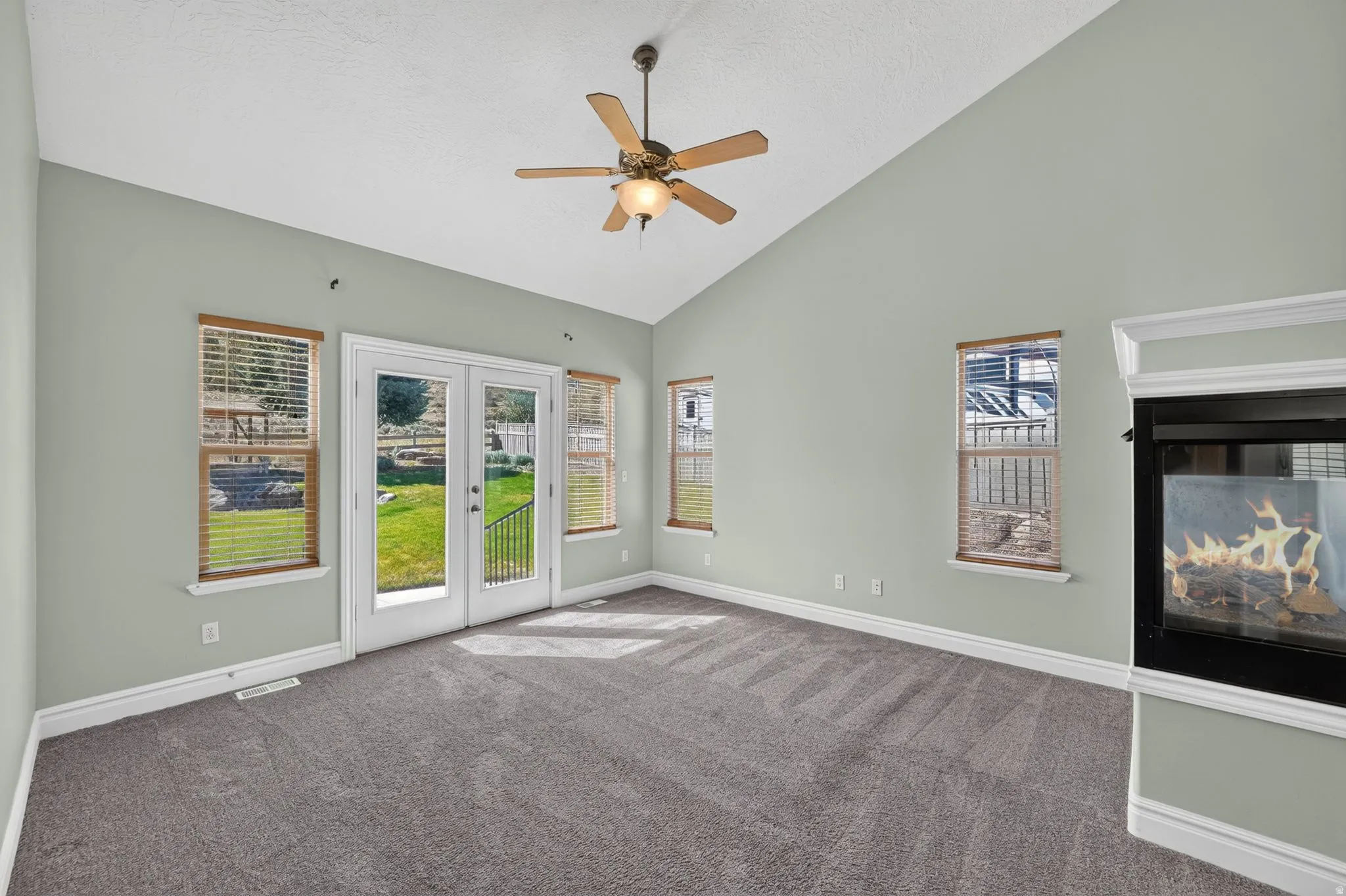 Spacious room featuring vaulted ceilings, a ceiling fan, and a built-in fireplace with a white mantel