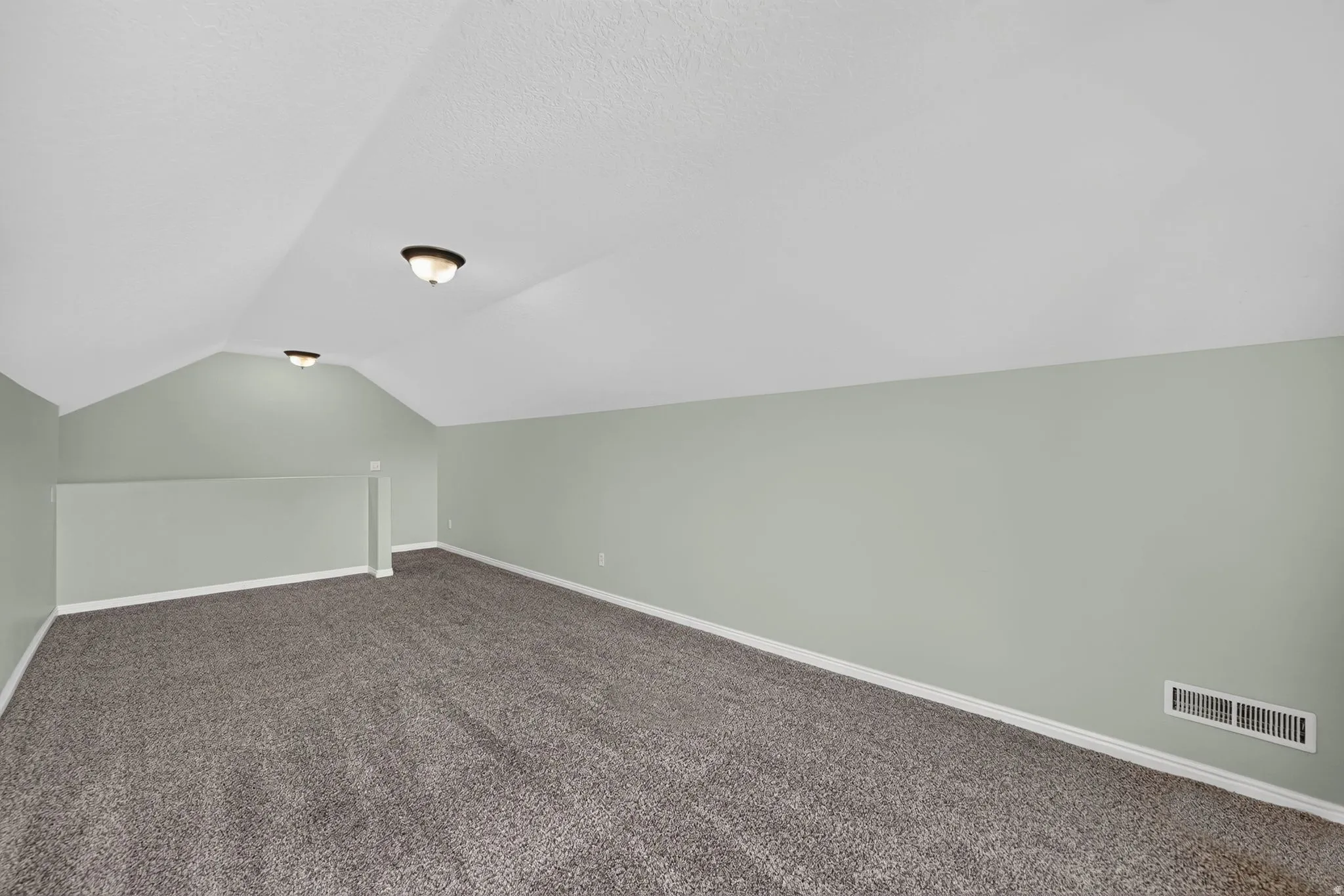 Spacious room featuring vaulted ceilings, light green walls, and dark gray carpeting