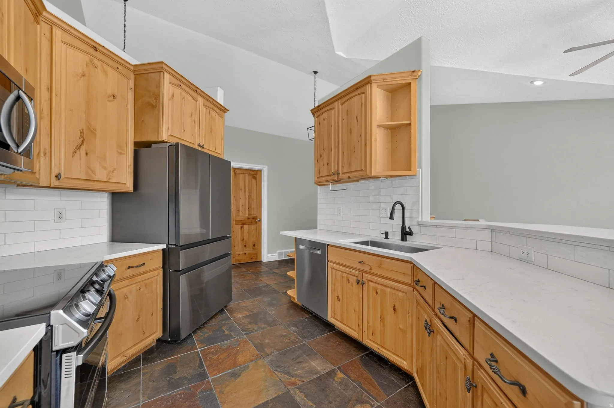 Kitchen featuring light wood cabinetry, white subway tile backsplash, white countertops, and stainless steel appliances