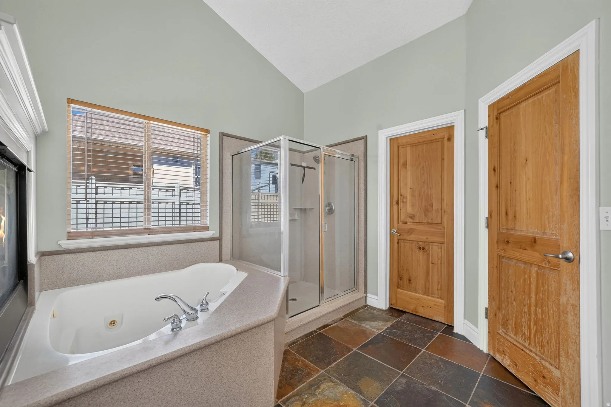 Bathroom featuring a corner jetted soaking tub with a tiled surround, a glass-enclosed shower, and natural wood doors