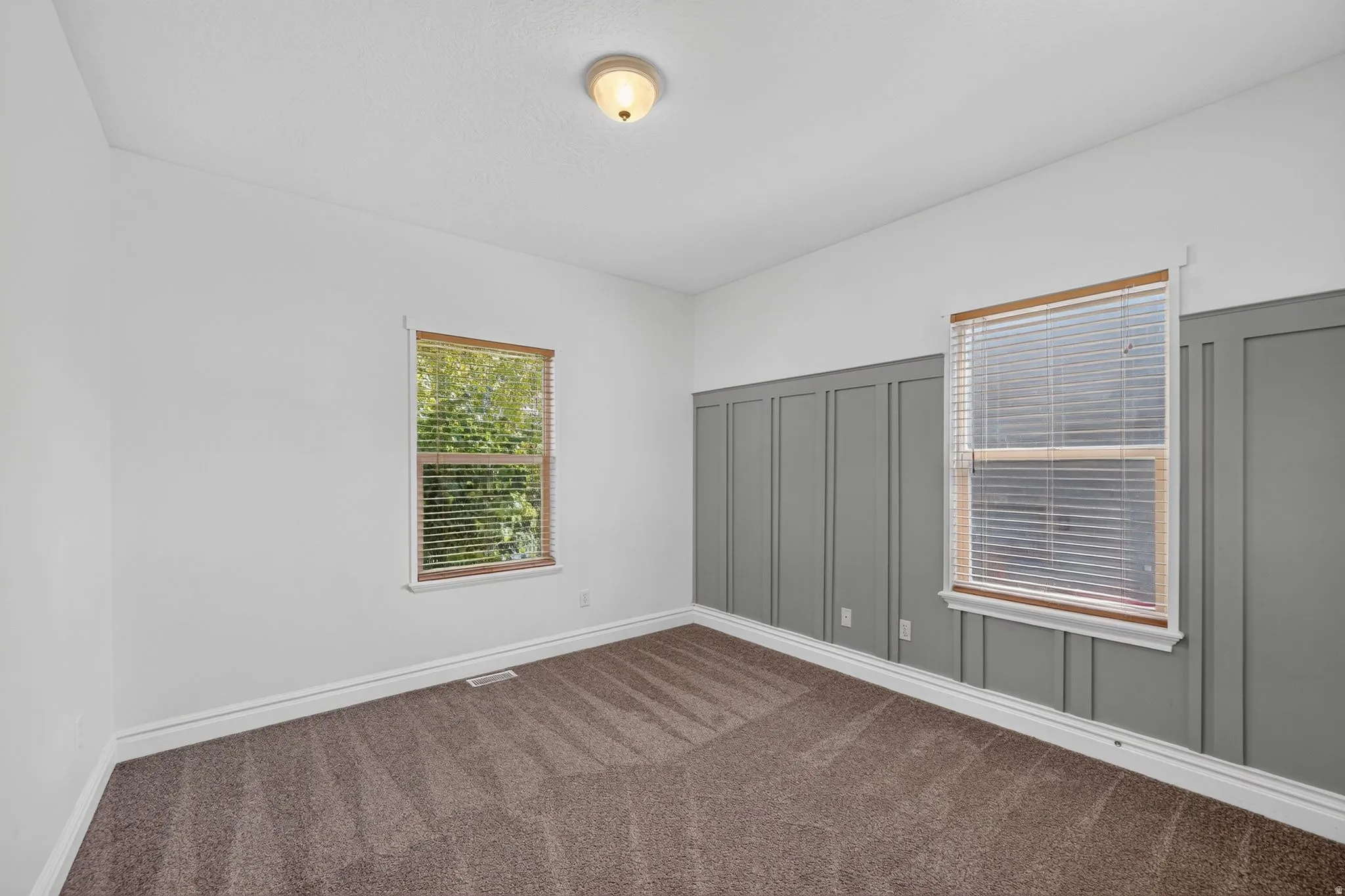 Room featuring board and batten accent wall, neutral wall paint, two windows with blinds, wood-finish window trim, and carpet flooring