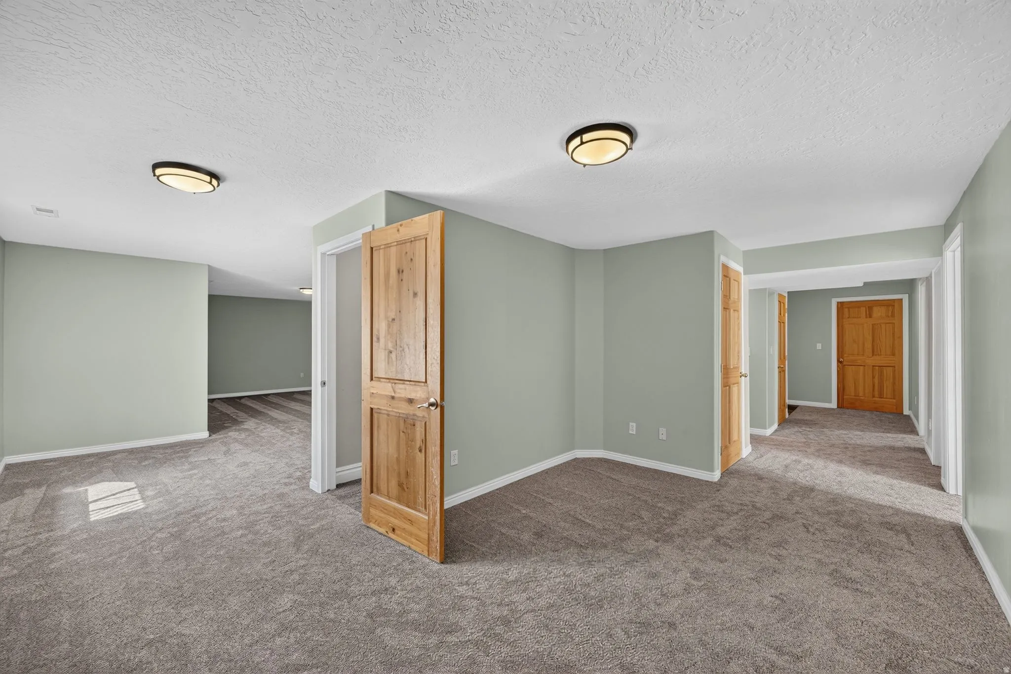 Hallway and common area with light green wall paint, textured ceilings, recessed lighting, wood-finish doors, and gray carpet flooring