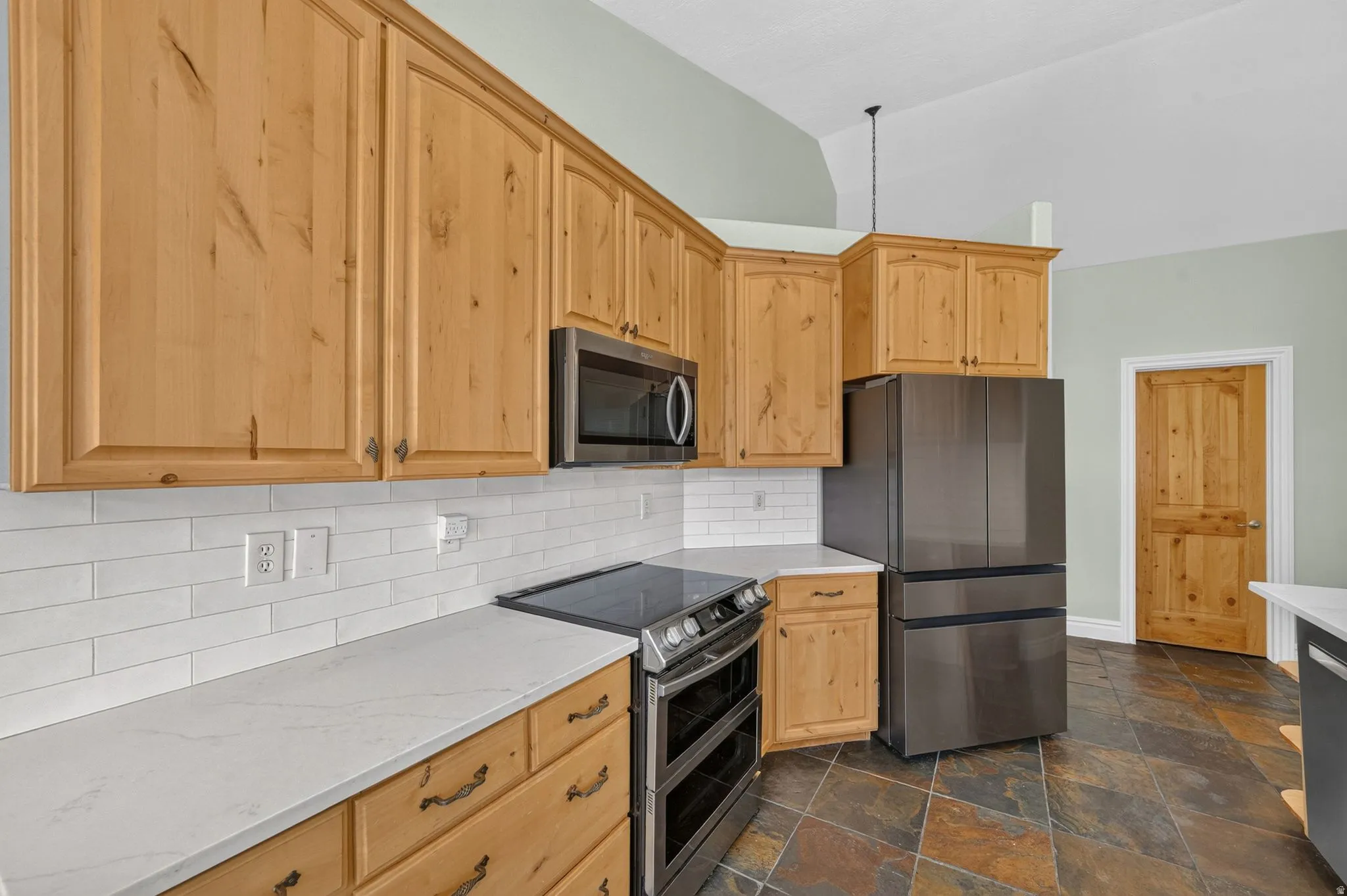 Kitchen featuring natural wood cabinetry, white subway tile backsplash, light-toned countertops, and dark slate floor tiles