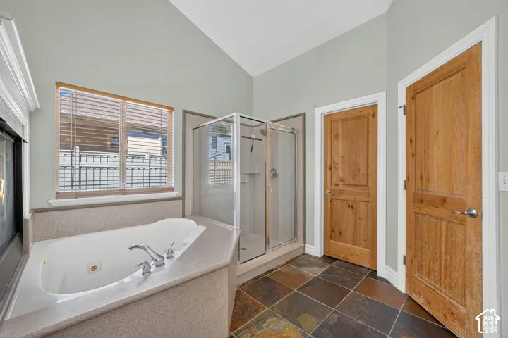 Bathroom featuring a corner jetted soaking tub with a tiled surround, a glass-enclosed shower, and natural wood doors