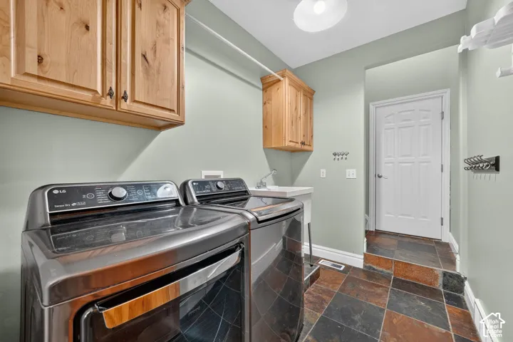 Utility room featuring wood cabinetry, a built-in utility sink, and durable slate tile flooring