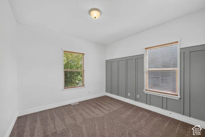 Room featuring board and batten accent wall, neutral wall paint, two windows with blinds, wood-finish window trim, and carpet flooring