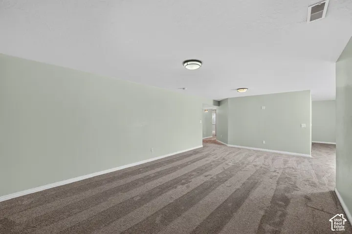 Spacious interior room featuring light-toned walls, textured ceiling, and flush-mount lighting fixtures
