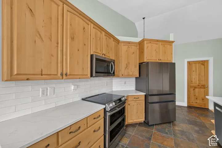 Kitchen featuring natural wood cabinetry, white subway tile backsplash, light-toned countertops, and dark slate floor tiles