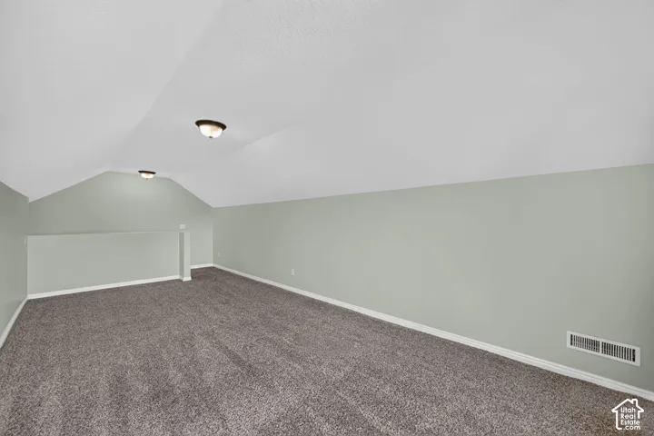 Spacious room featuring vaulted ceilings, light green walls, and dark gray carpeting
