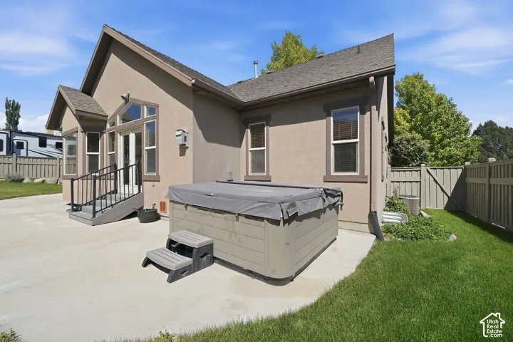 Rear exterior featuring a hot tub, concrete patio, and a staircase with black metal railings