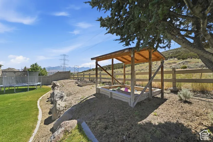 Expansive backyard featuring a natural rock retaining wall, a dedicated sandbox area with a wooden shade structure, a manicured lawn, and a wooden perimeter fence