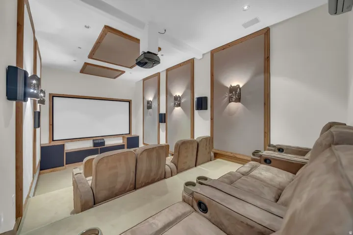 Dedicated media room featuring tiered seating, a large projection screen, built-in sound system, recessed lighting, and integrated wall sconces