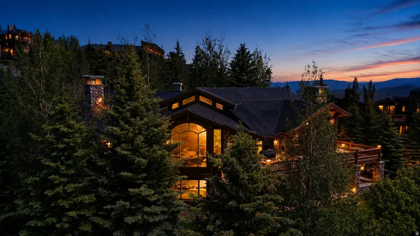 Multi-level property featuring a prominent arched picture window, stone chimney, and a spacious wooden deck