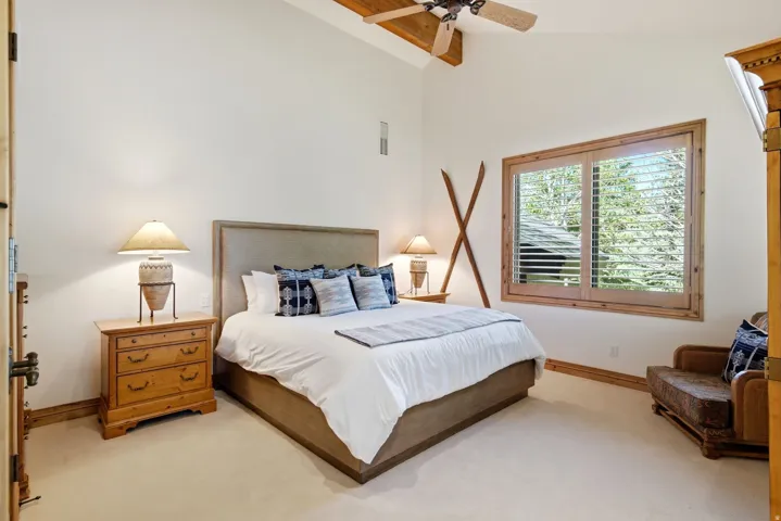 Bedroom featuring vaulted ceilings with exposed wood beams, a ceiling fan, and light-toned carpeting