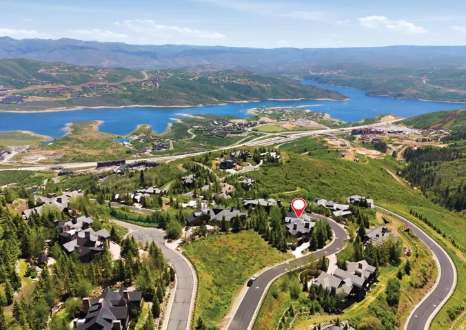 Expansive hillside property featuring a multi-level residence, dense natural landscaping, paved winding roadways, and a prominent distant lake