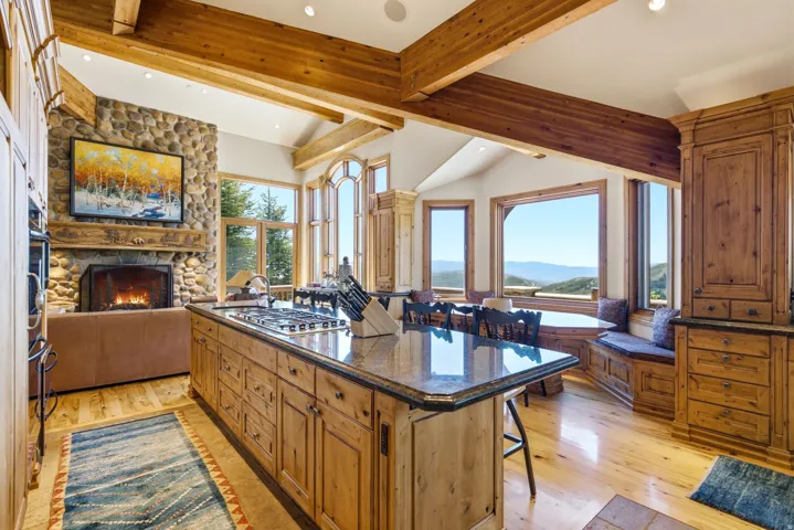 Kitchen featuring a center island, hardwood flooring, stone fireplace, exposed wood beams, and a dining area with built-in bench seating