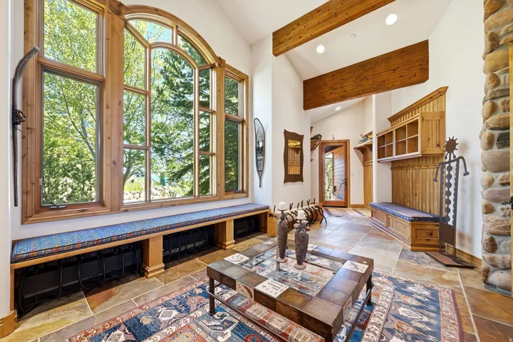 Expansive arched window with wood framing, built-in window bench, exposed wood beams, natural stone flooring, and a stone wall accent