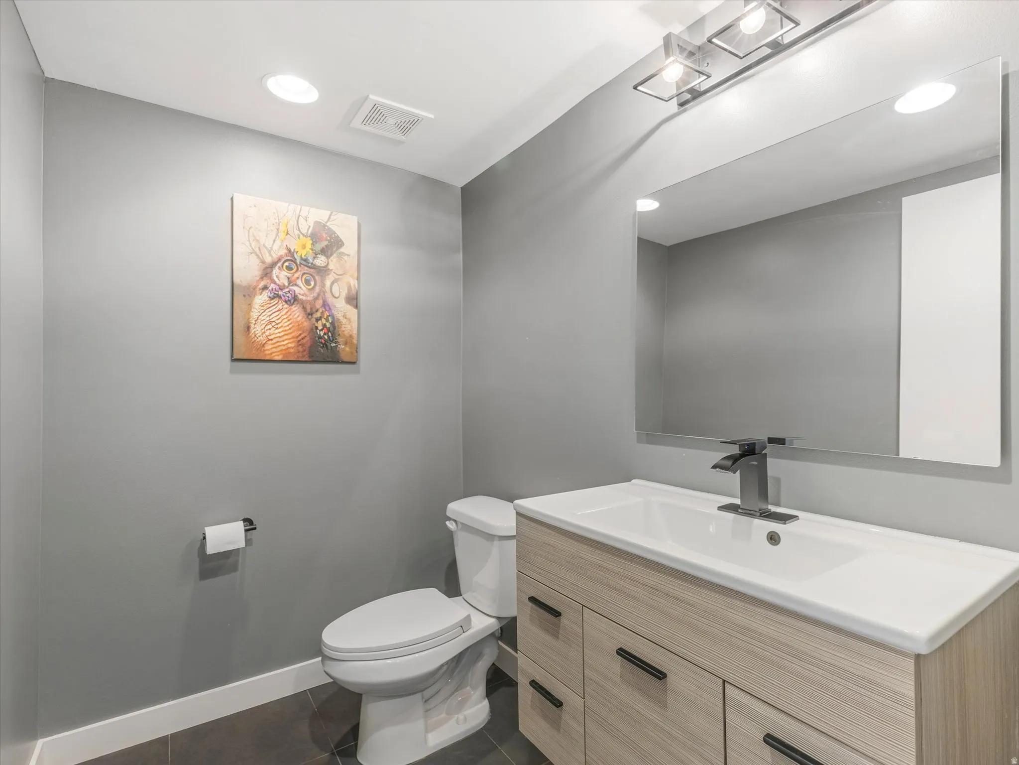 Contemporary bathroom featuring a light wood-finish vanity with an integrated white sink, a sleek black faucet, and a wall-mounted rectangular mirror