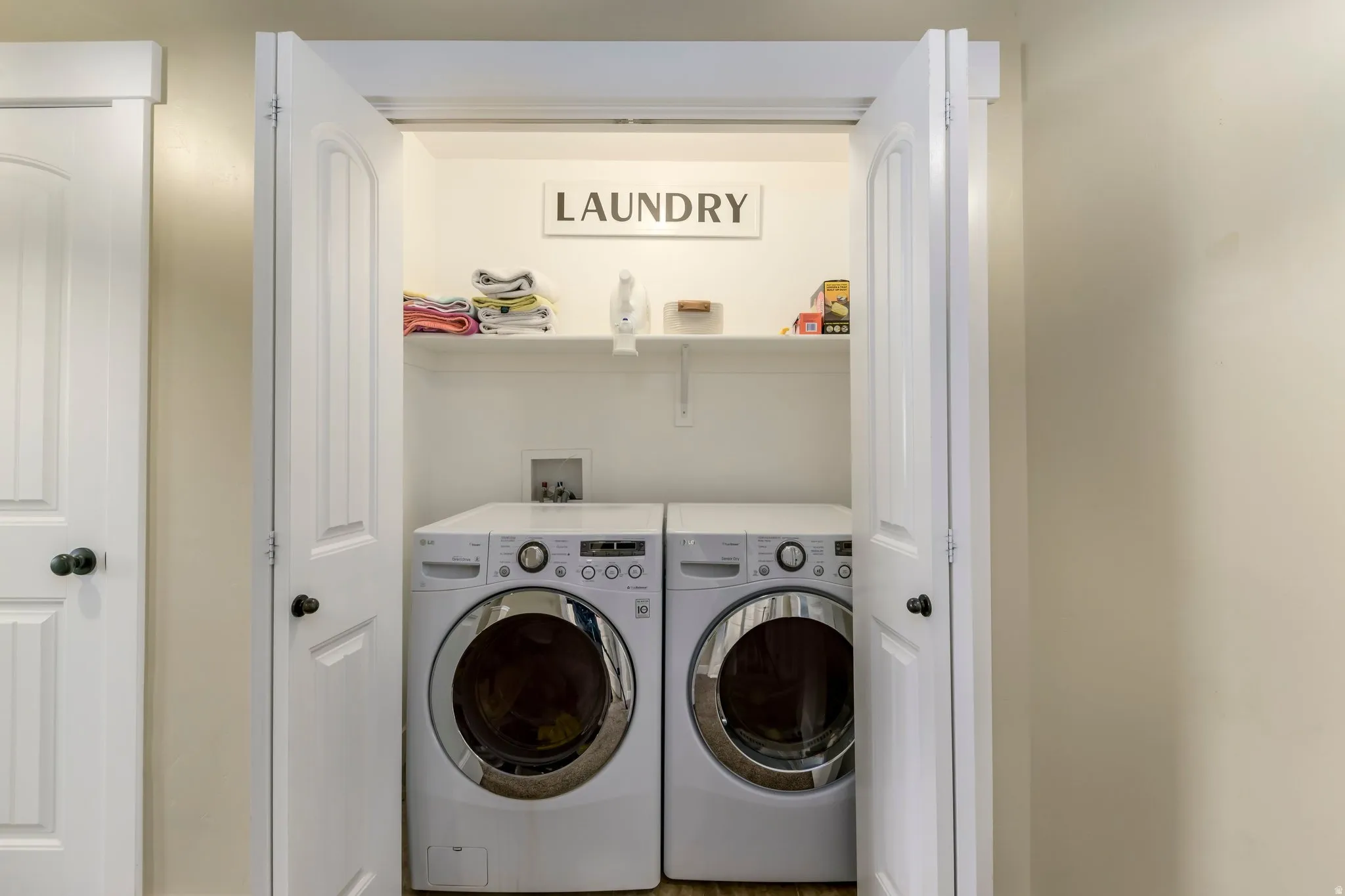 Dedicated laundry closet featuring a white front-load washer and dryer set, a high shelf for storage, and bi-fold doors