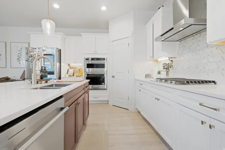 Modern kitchen featuring light wood-finish flooring, white cabinetry with contemporary hardware, stainless steel appliances including a built-in oven and microwave, and a gas cooktop with a coordinating range hood