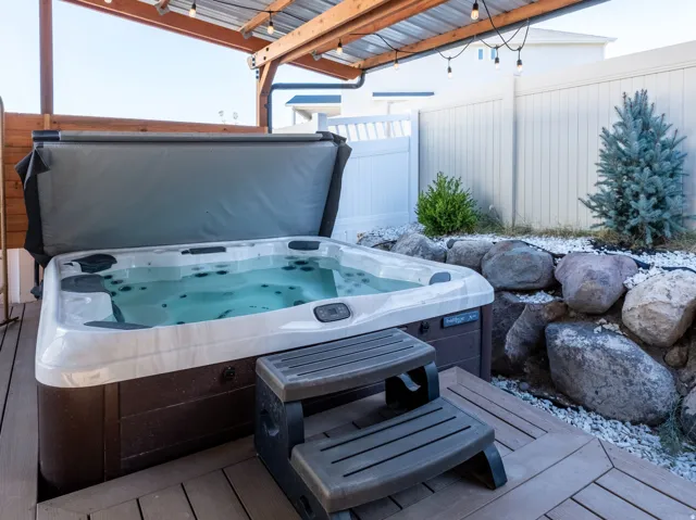 Outdoor spa on a composite deck under a wooden pergola with string lights