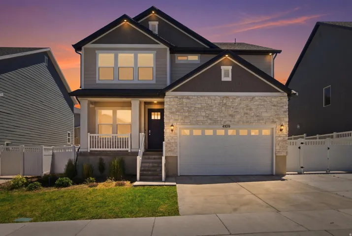 Modern two-story residence featuring a stone and siding exterior, two-car garage with transom windows, covered porch with white railing, and a dark entry door with frosted glass inserts