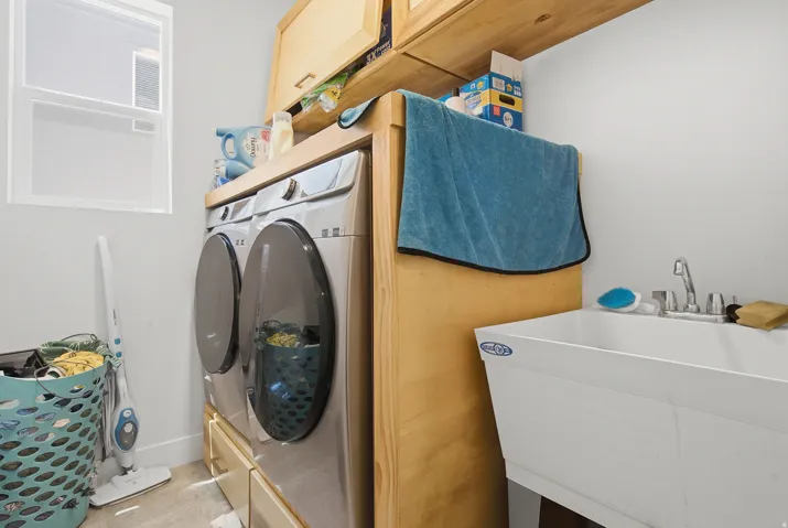 Dedicated laundry area featuring a utility sink with dual-handle faucet, wood-finish cabinetry, and a window for natural light