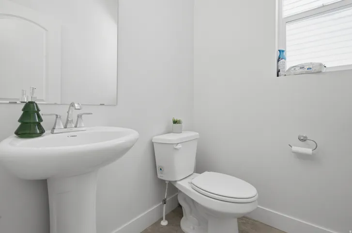 Pedestal sink with chrome faucet, a white toilet, and a window with horizontal blinds