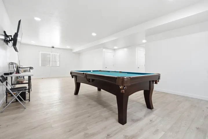 Spacious recreation room featuring light wood-finish flooring, recessed lighting, and bright white walls
