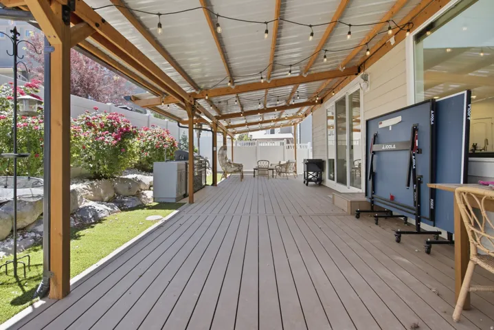 Expansive covered outdoor deck featuring a corrugated roof, exposed wood beams, and string lighting