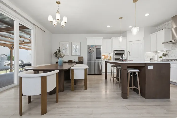 Open-concept kitchen and dining area featuring light wood-finish flooring, a kitchen island with seating, pendant lighting, white cabinetry, and stainless steel appliances