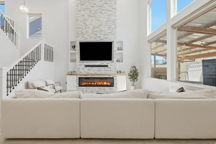 Vaulted living area featuring a floor-to-ceiling stacked stone fireplace, an integrated media niche, large picture windows, and a staircase with open black metal balusters