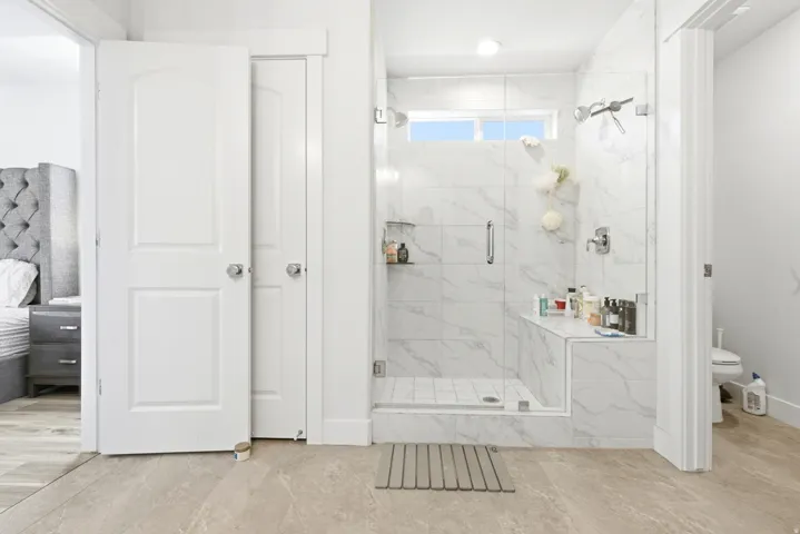 Spacious walk-in shower featuring large format marble-look tile, a glass enclosure, and a built-in bench