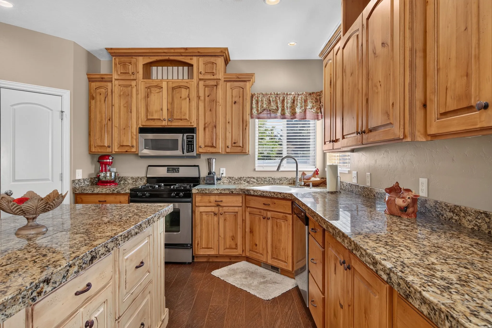 Kitchen featuring a gas range, stainless steel appliances, granite countertops, wood-finish flooring, and natural wood cabinetry