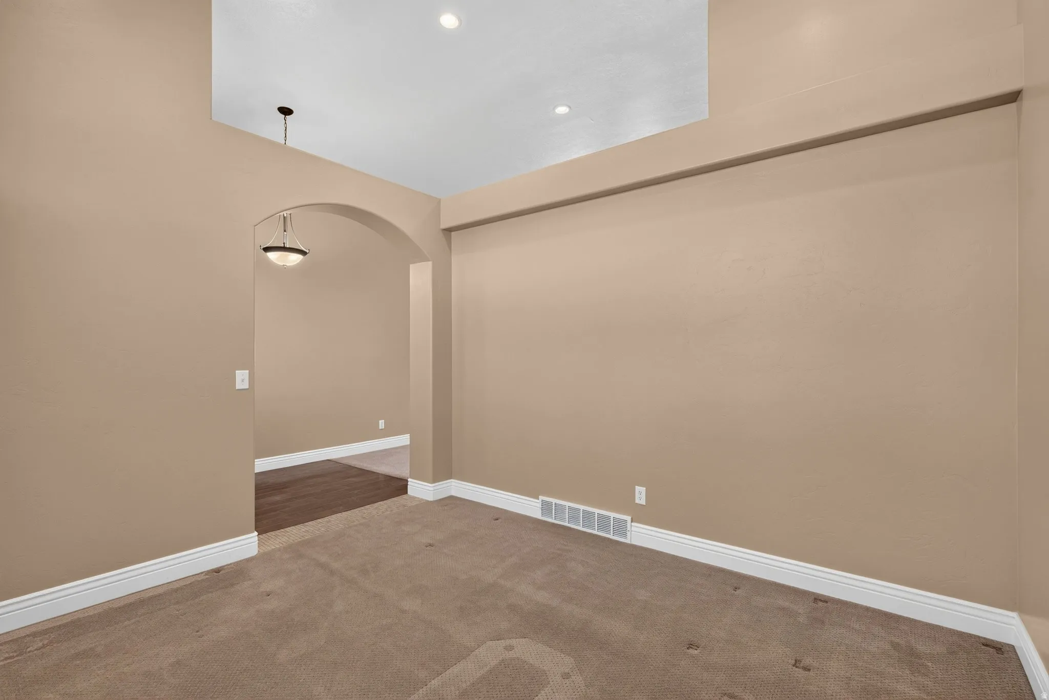 Spacious room featuring vaulted ceilings, recessed lighting, an arched doorway, and carpet flooring