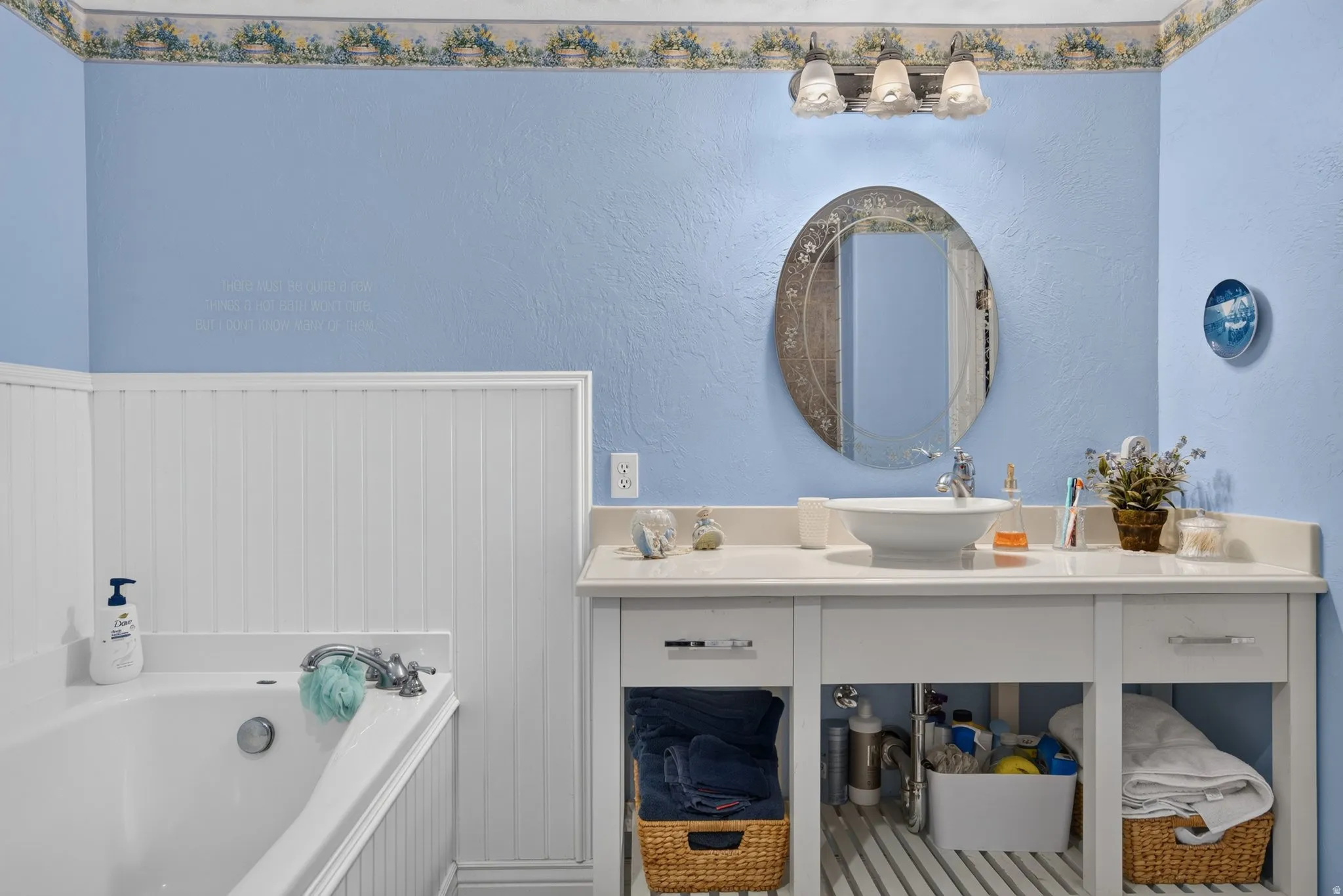 Bathroom featuring a built-in tub with white paneling surround, a white vanity with a rectangular countertop, and an oval mirror with an ornate frame