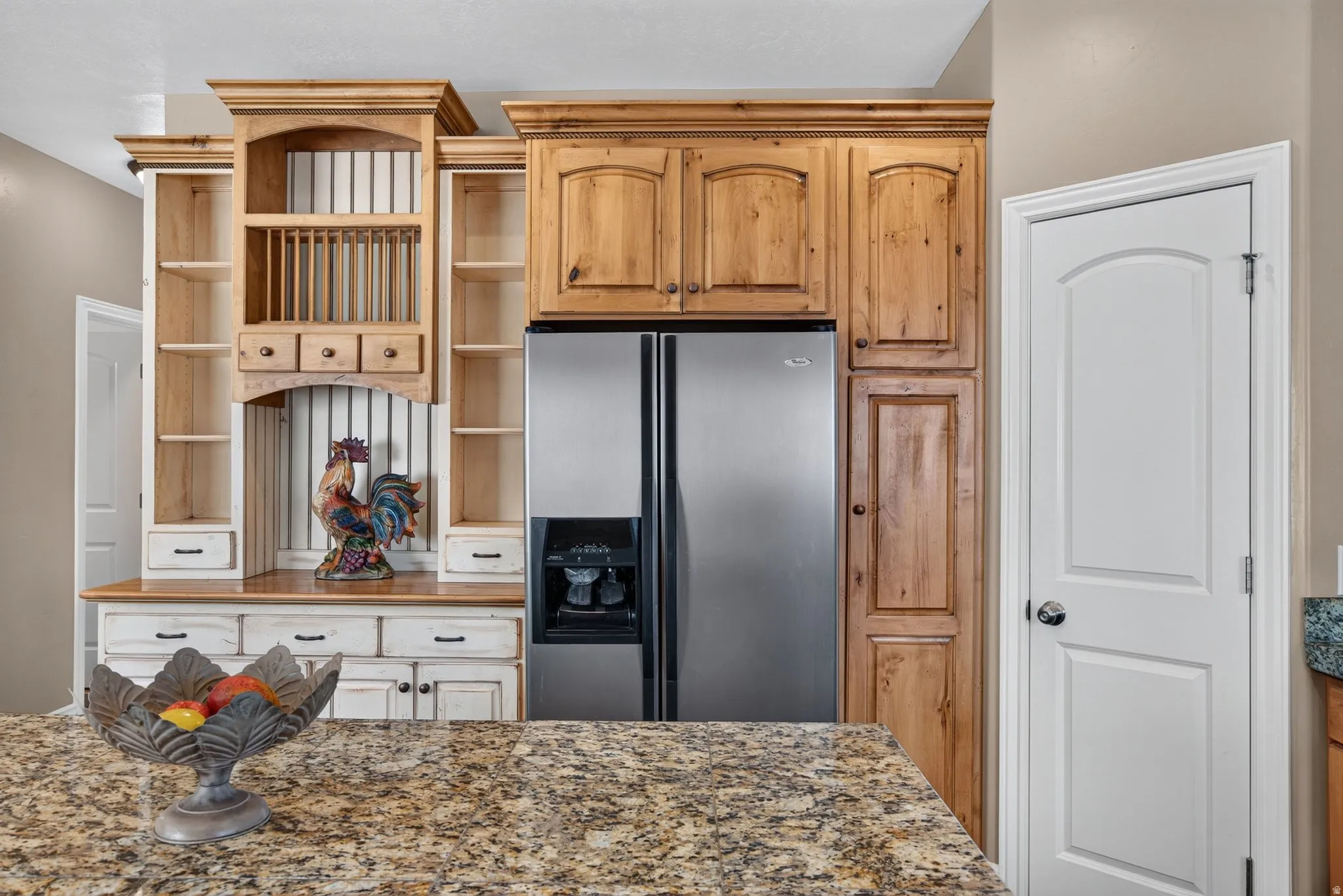 Kitchen featuring granite-style countertops, stainless steel refrigerator, custom wood cabinetry, integrated plate rack, and white paneled doors