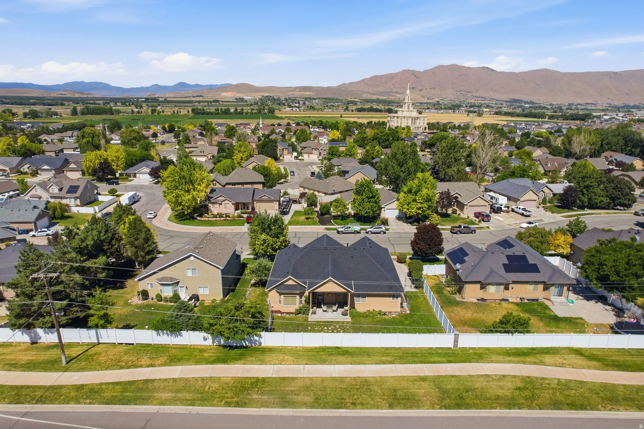 Residential street with a white privacy fence, mature trees, and mountain backdrop