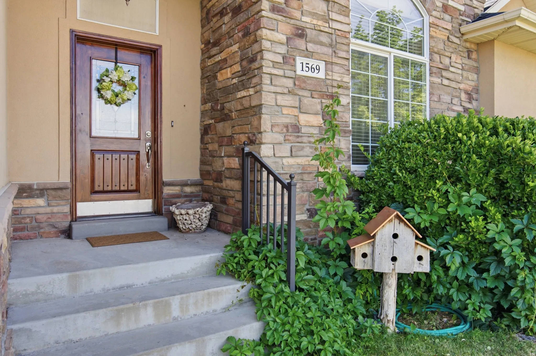 Front entry featuring a wood door with decorative glass inserts, concrete steps with an iron handrail, and a stone facade