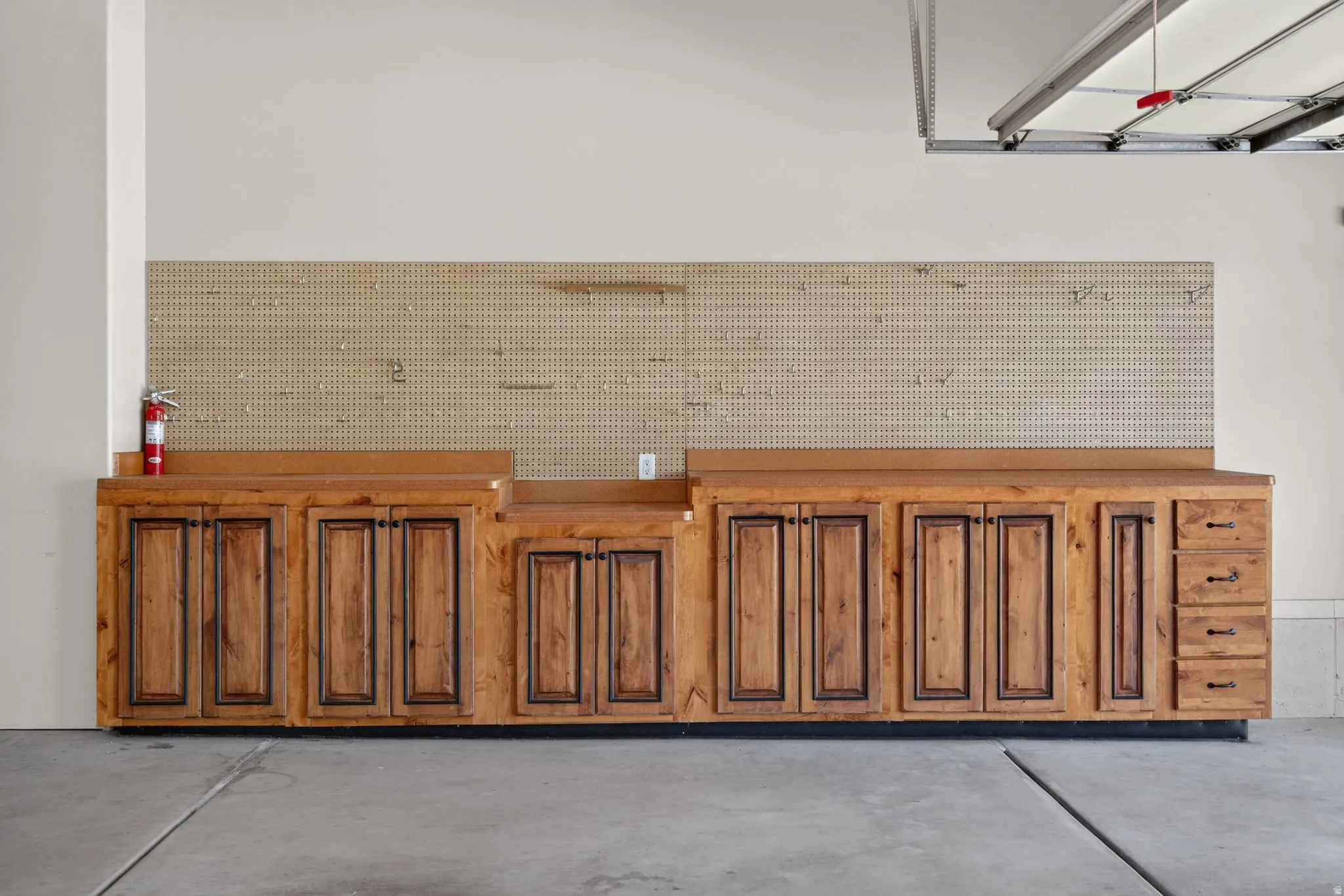 Garage featuring extensive built-in wooden cabinetry, integrated work surfaces, a pegboard wall system, and concrete flooring