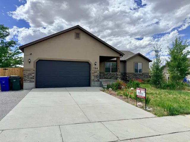 Contemporary ranch-style home featuring a two-car garage, stone veneer accents, stucco exterior, covered entry, and mature landscaping