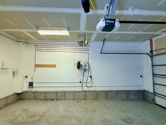 Garage with concrete flooring, fluorescent overhead lighting, an exposed ceiling, and a garage door opener system