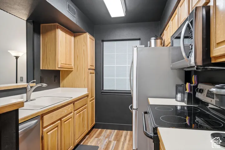 Kitchen featuring natural wood cabinetry, white countertops, stainless steel appliances, and a window with blinds