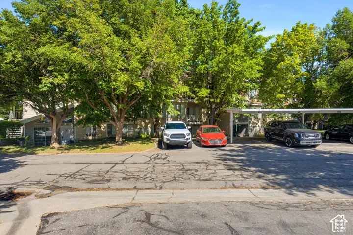 Exterior building with mature trees, carport parking, and visible apartment balconies