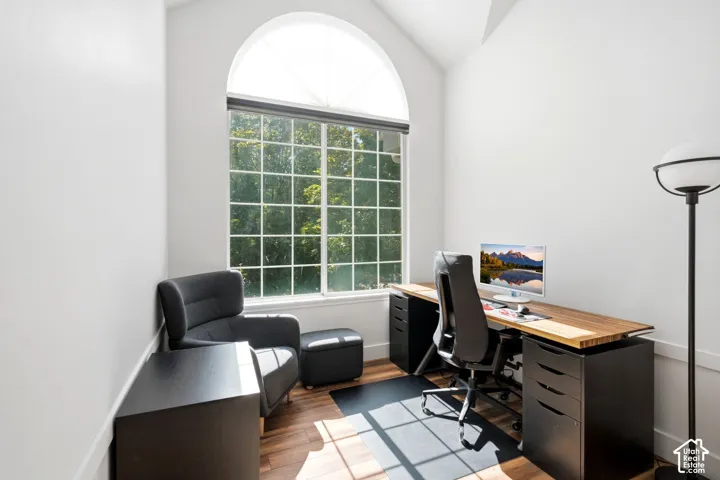 Dedicated office space featuring vaulted ceilings, wood-finish flooring, and a large arched window with a transom