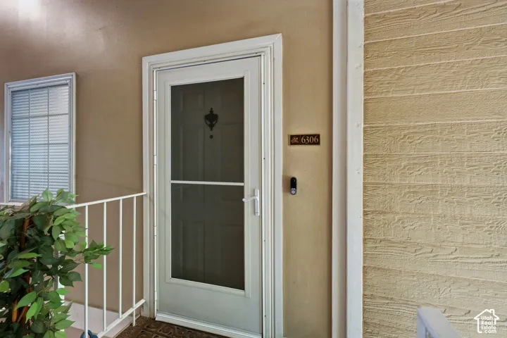 Entryway featuring a white storm door, beige stucco exterior, and a discrete house number plaque