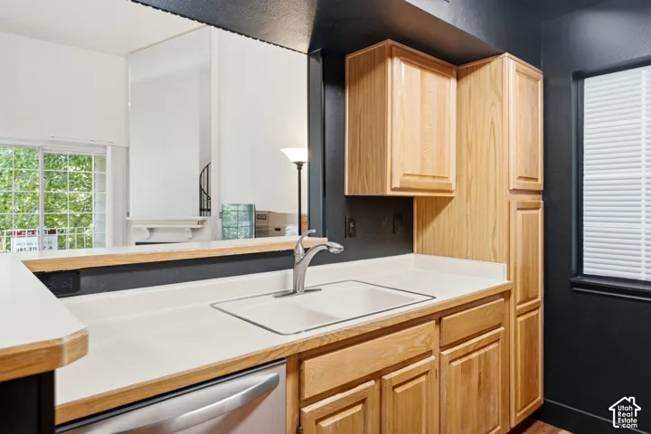 Kitchen featuring light wood cabinetry, a stainless steel sink with a single-handle faucet, light-toned countertops, and a built-in dishwasher