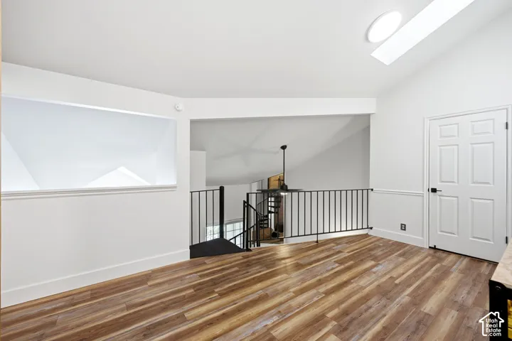 Open loft area featuring wood-finish flooring, white vaulted ceilings, and a skylight