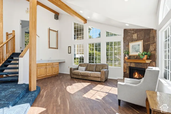 Vaulted ceiling living area featuring exposed wood beams, a stone-clad fireplace, and multiple large windows with muntins