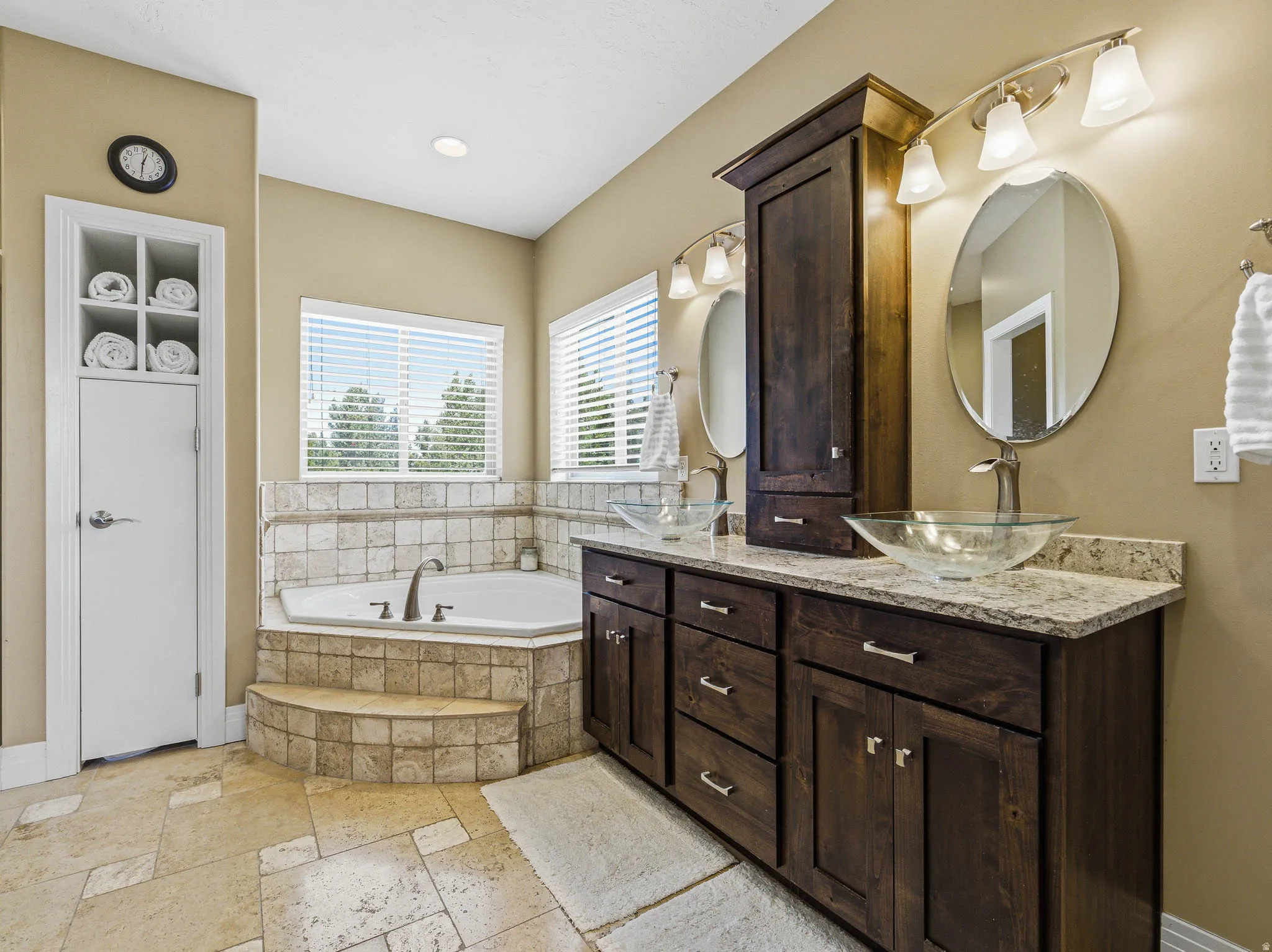 Bathroom featuring a corner soaking tub with tiled surround, double vanity with granite-style countertops, dark wood-finish cabinetry, and vessel sinks